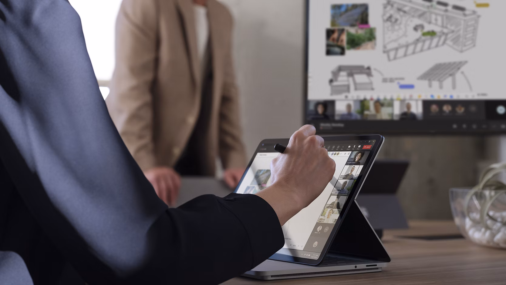 A person writes on the screen of a Surface device while the image is projected on the Surface Hub 3 for Business. 