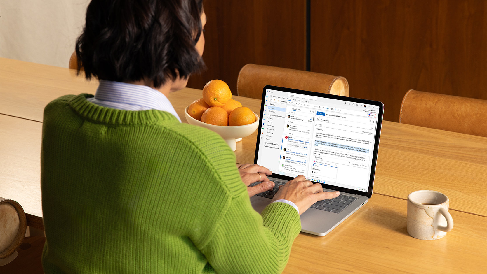 A person uses Microsoft Outlook on a laptop while sitting at a kitchen table.