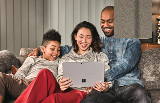 A family, sitting on a couch, using a Surface laptop together.