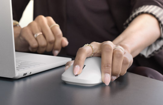 A left-handed person uses Surface Mouse (2nd Edition) with a Surface device.