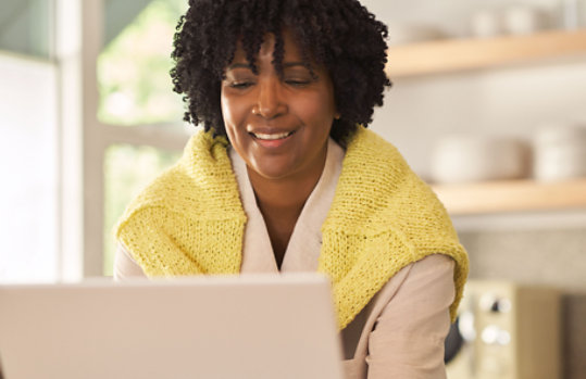 A smiling woman in a yellow jumper types on her laptop screen. 