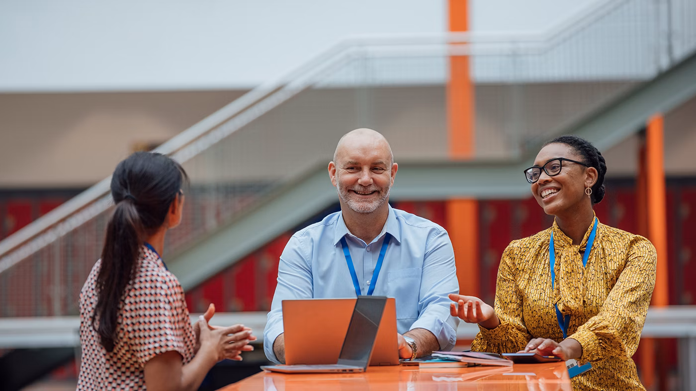 Three teachers sitting at a table, having a discussion in the lobby area of their school