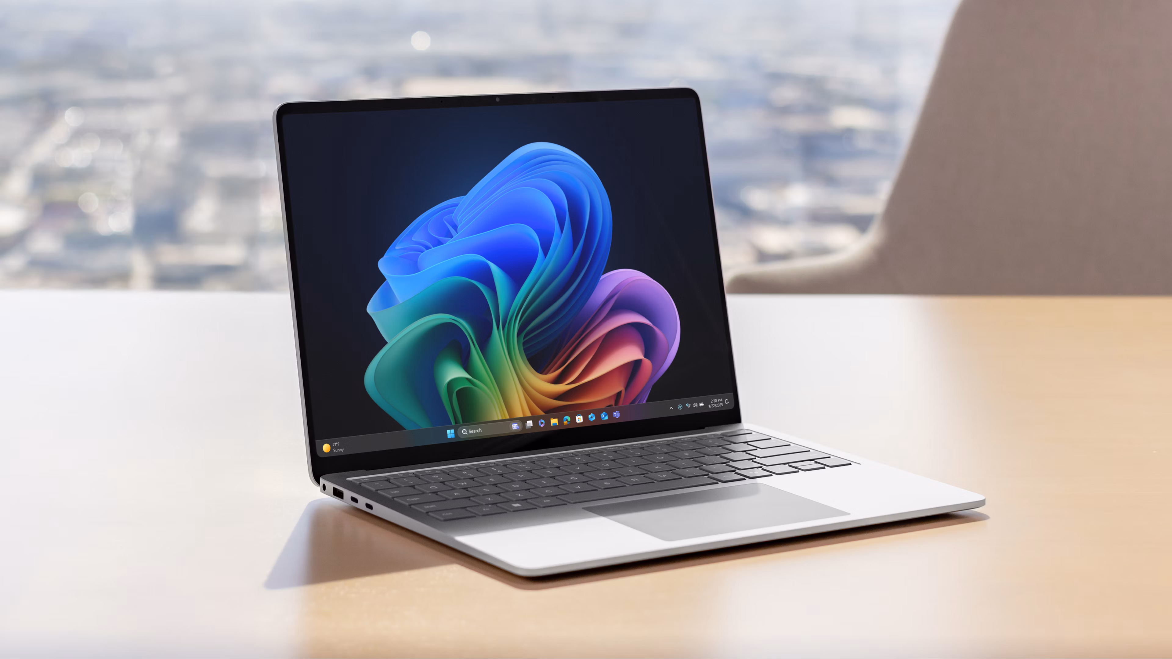 Een open Surface Laptop met een levendig, anti-reflecterend PixelSense™-scherm met een afbeelding van een regenboogbloem op een bruin bureau met een stoel en een stadsgezicht op de achtergrond.