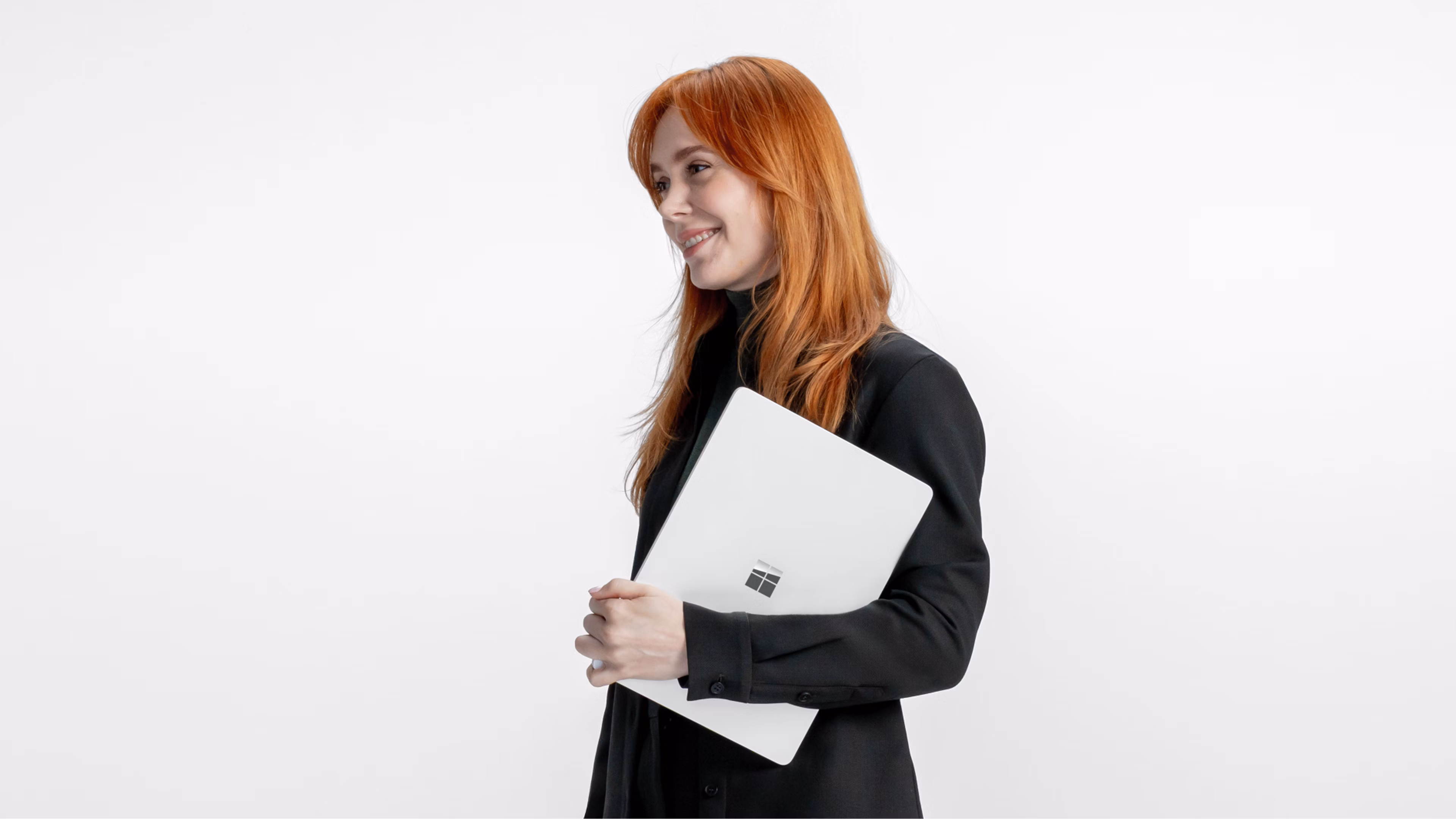 Een glimlachend persoon die naar links kijkt met een gesloten chromen Surface Laptop tegen een grijze achtergrond